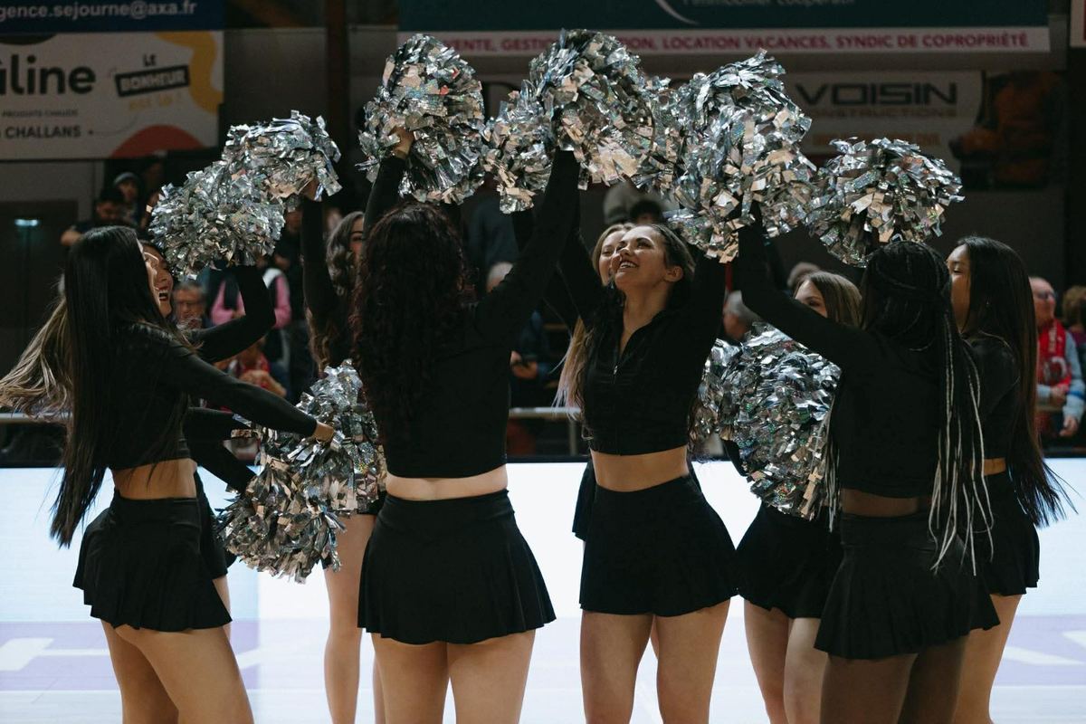Pompons argentés levés, danseuses en noir face au public